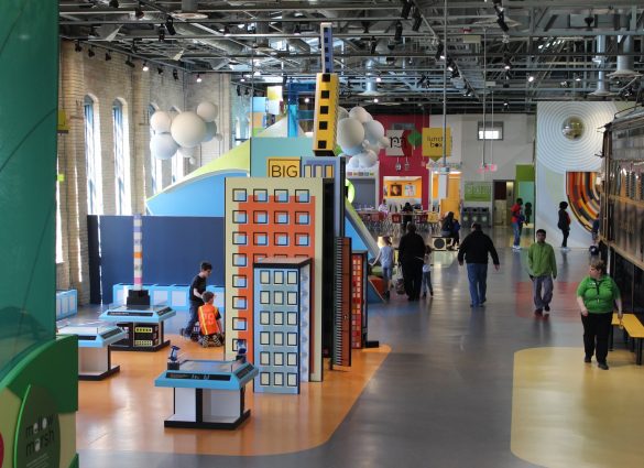 Inside a children's museum with colorful displays, kids playing, and people walking around.