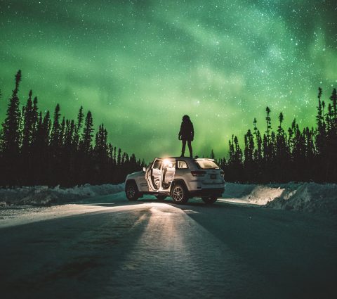 A person standing on a car watching the northern lights in The Pas