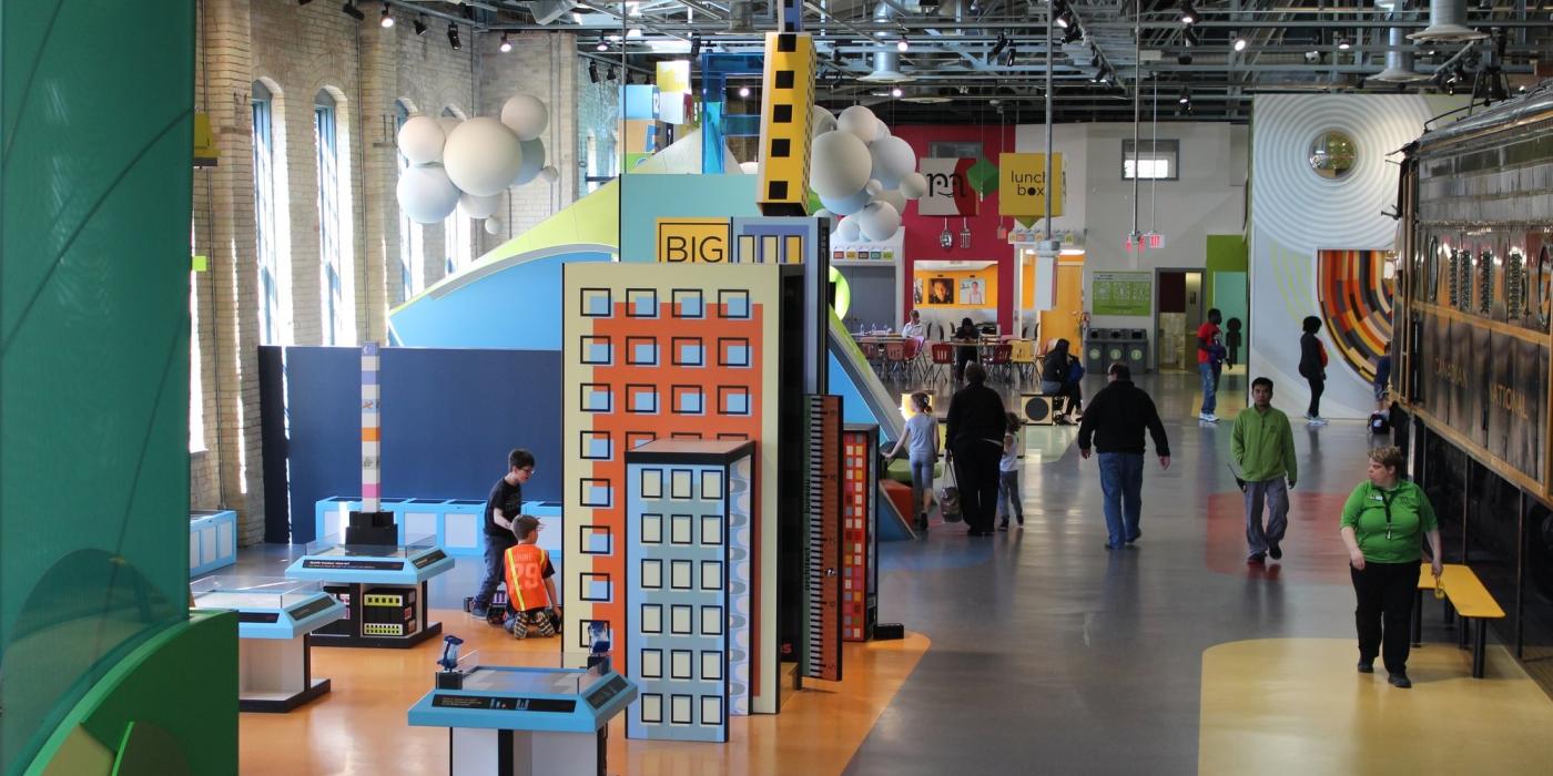Inside a children's museum with colorful displays, kids playing, and people walking around.