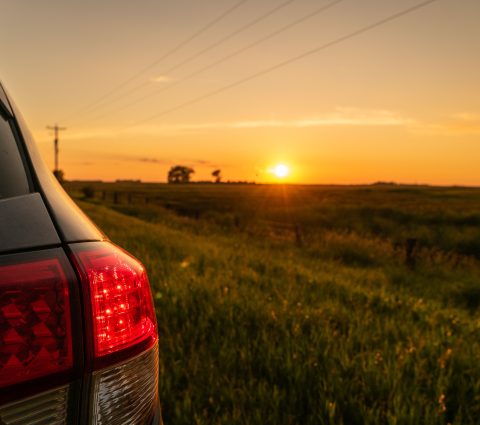 Looking past the tail lights on a car at the sunset over a farm field.